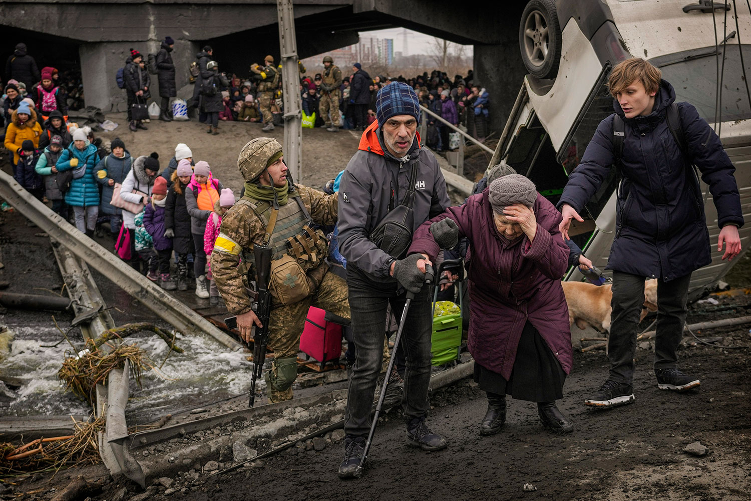 En eldre kvinne blir hjulpet over elven Irpin på en improvisert bro etter at hovedbrua var blitt sprengt i stykker i et russisk angrep i mars 2022.