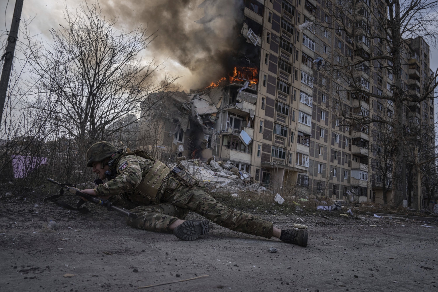 En ukrainsk politimann søker dekning foran en brennende bygning i Avdijivka i Ukraina i 2023.